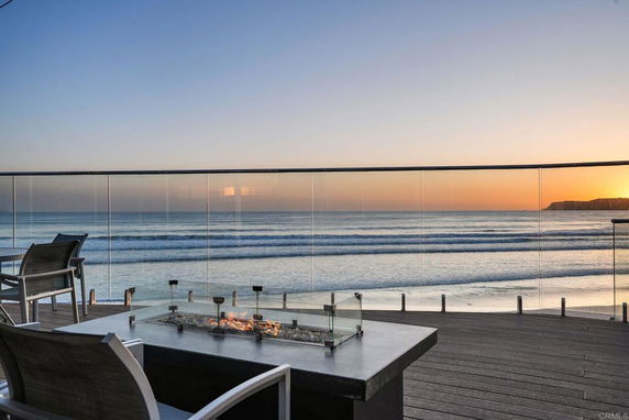 Panoramic view of the ocean from a balcony with glass railing and outdoor seating.