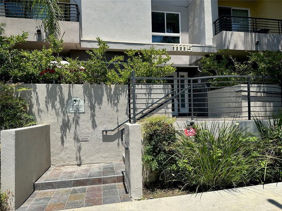 Exterior view of a modern multi-story building entrance with balconies and plants.