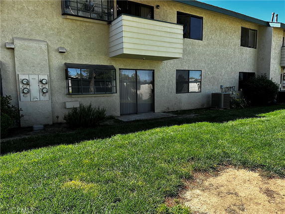 Rear view of a two-story apartment building with balconies and grass lawn.