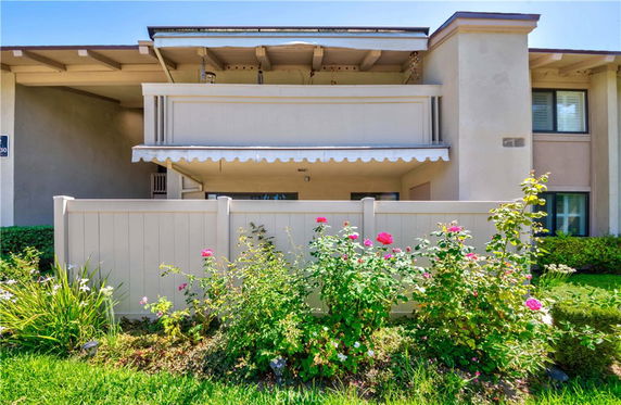 Front view of a two-story residential building with a balcony and a fenced garden area.