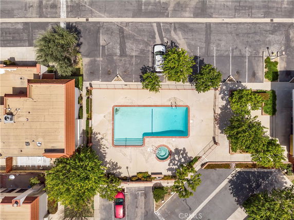 Aerial view of a swimming pool and surrounding area with parking and greenery.