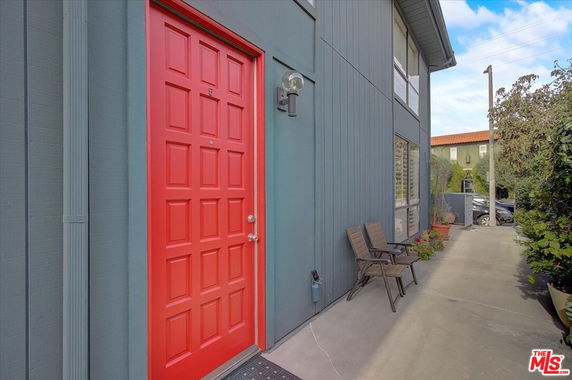 Exterior view of a building with a prominent red door and blue siding, featuring windows and outdoor seating.
