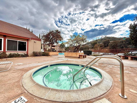 Outdoor swimming pool area with a small circular hot tub beside a building.
