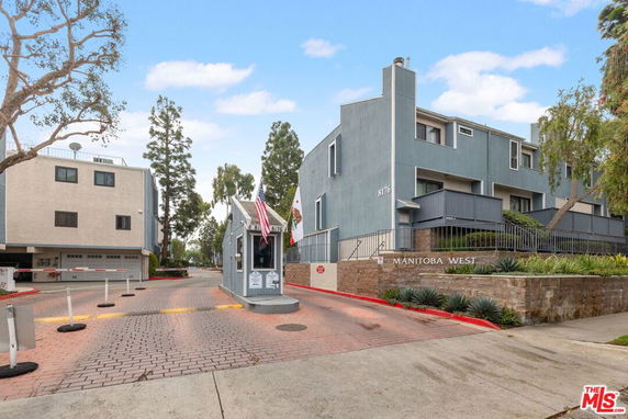Front view of a multi-story residential building with an entrance gate and guard booth.