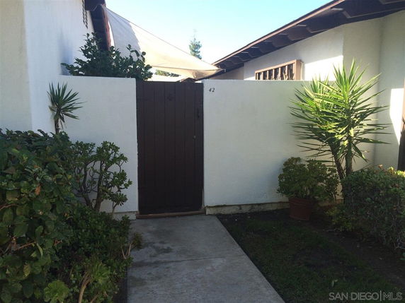 Front view of a house with a tall wooden gate and white walls.