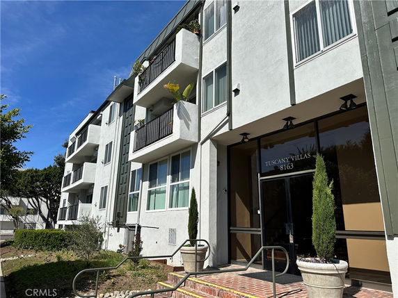 Front view of a multi-story apartment building named Tuscany Villas with balconies and a glass entrance door.