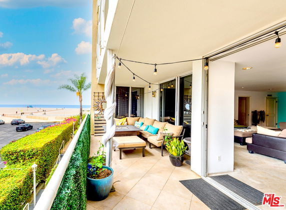 Outdoor balcony with seating area overlooking a beach and ocean.