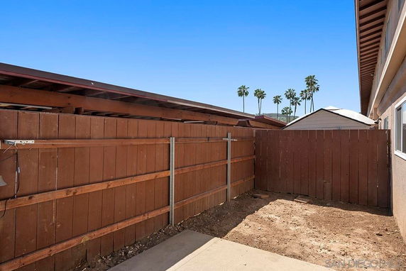 Enclosed outdoor area with a wooden fence and view of palm trees.