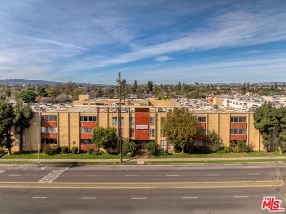 Front view of a multi-story apartment building with trees and a road in front.