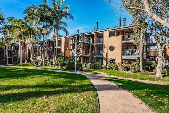 Front view of a multi-story apartment building with balconies and palm trees.
