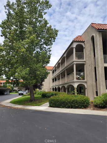 Front view of a three-story residential building with arched balconies and tiled roof.