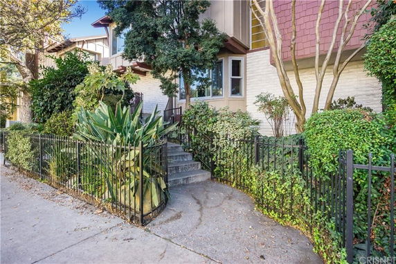 Front view of a multi-story townhouse with brick and paneling, surrounded by trees and shrubbery, and accessed by concrete steps.
