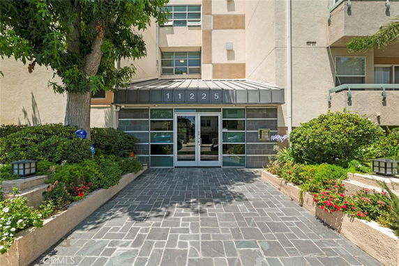 Front view of a multi-story building entrance with glass doors and stone pathway.