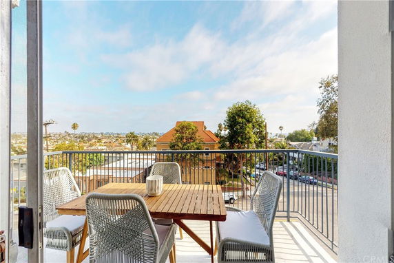 Outdoor balcony with a wooden table and chairs overlooking a neighborhood.