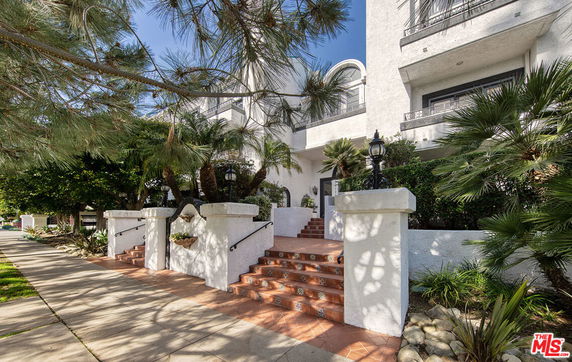 Front view of a multi-story building with decorative entrance steps and lush greenery.