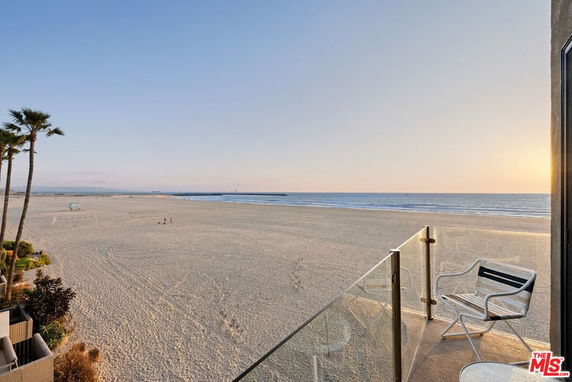 Balcony view overlooking a beach and ocean at sunset.