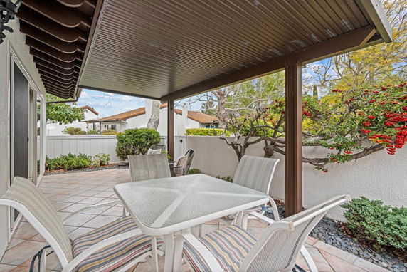 Patio with a table and chairs under a roof, surrounded by a fence and garden.