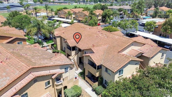 Aerial view of an apartment complex with red-tiled roofs and nearby greenery.