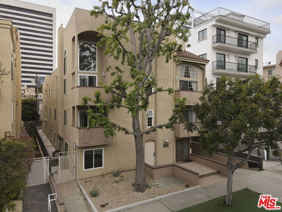 Front view of a beige multi-story residential building with several large windows and a gated entrance.