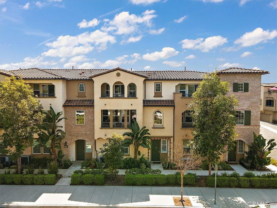 Front view of a multi-story residential building with a mix of brick and stucco exterior, featuring arched windows and a tiled roof.