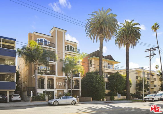 Front view of a multi-story apartment building with balconies and palm trees.
