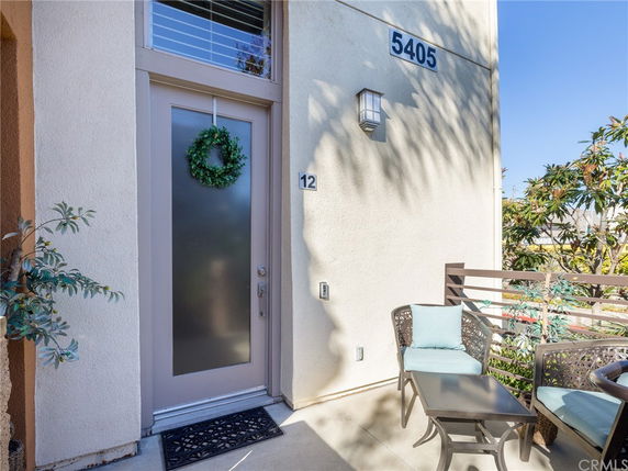 Front view of a modern house entrance with a frosted glass door, house number 5405, and a small outdoor seating area.