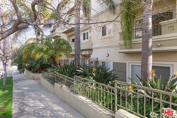 Front view of a multi-story residential building with balconies and surrounding greenery.