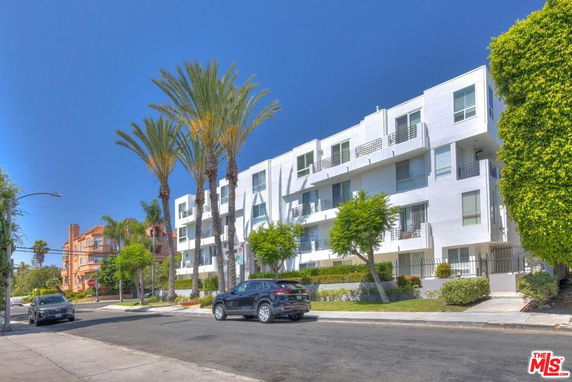 Front view of a modern multi-story building with balconies and palm trees.