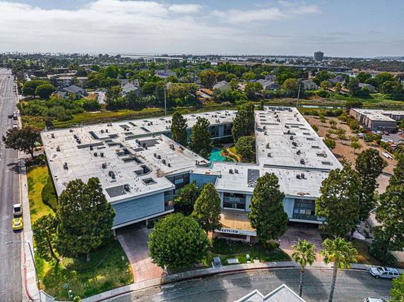 Aerial view of a large, multi-wing building complex with a flat roof and surrounded by trees and roads.