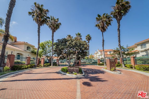 Front view of a residential complex with palm trees and a brick driveway.