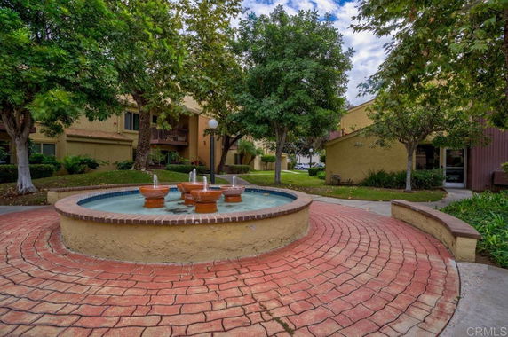 An outdoor area with landscaped gardens, trees, and a decorative water fountain.