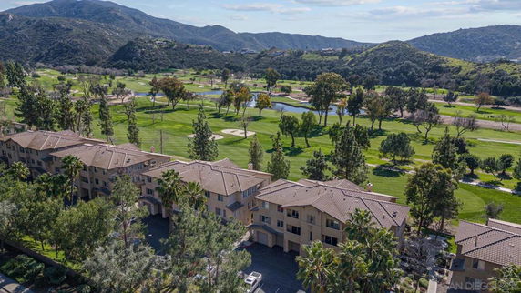 Aerial view of a row of residential buildings with a golf course and mountainous landscape in the background.