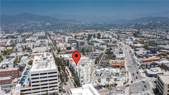 Aerial view of a cityscape with multiple buildings and streets, mountains in the background.