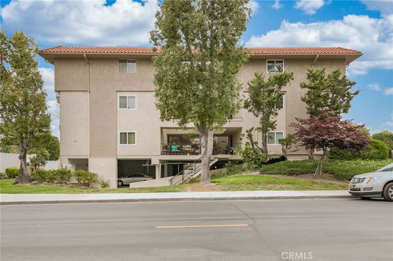 Front view of a multi-story residential building with trees and a driveway.