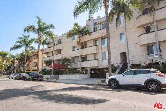 Front view of an apartment building with multiple floors and palm trees.
