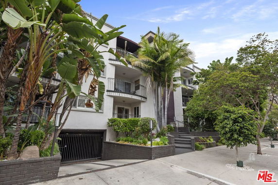 Front view of a multi-story building with balconies and surrounded by trees.