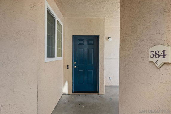 Entrance of a building with a dark blue door and beige walls, featuring a window and an address plaque with the number 384.