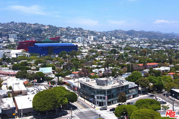 Panoramic view of a cityscape with various buildings and a hilly backdrop.