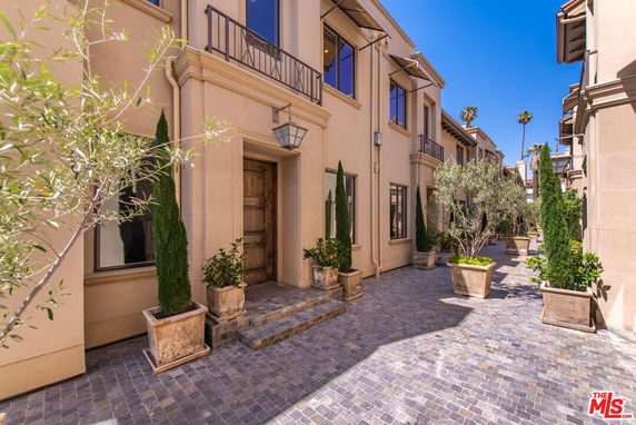 Front view of a multi-story building with large windows and potted plants along a cobblestone path.