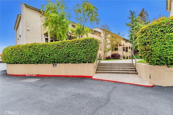 Front view of a multi-story building with hedges and steps leading up to it.