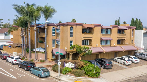 Front view of a three-story apartment building with balconies and a parking area.