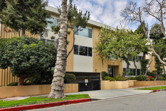 Front view of a multi-story residential building with trees in front.