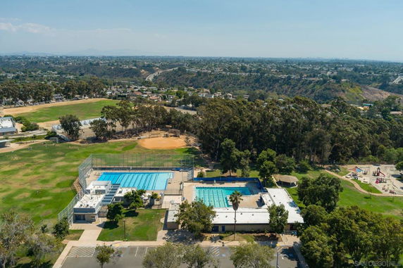 Aerial view of a facility with two swimming pools and adjacent buildings surrounded by trees.