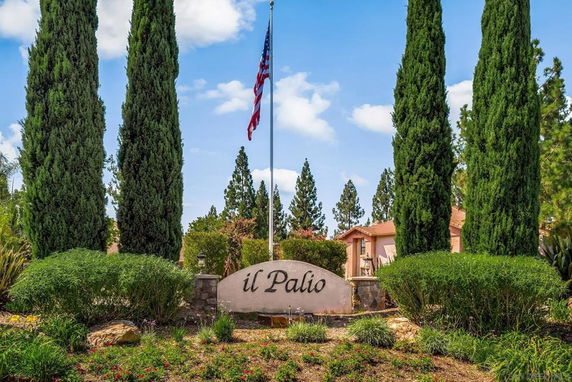 Entrance sign of a residential complex with tall trees and an American flag.