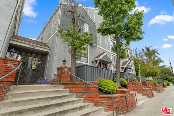 Front view of a multi-story residential building with brick steps and trees.
