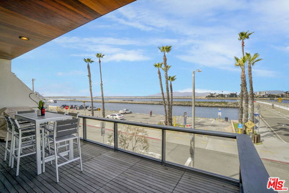 Outdoor balcony with a seating area overlooking the waterfront and palm trees.