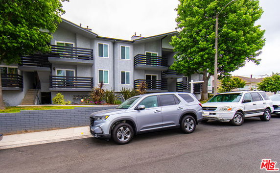 Front view of a two-story residential building with balconies and parked cars in front.