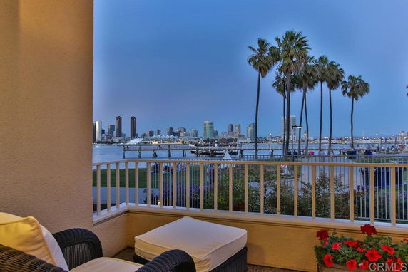 View of the city skyline and waterfront from a building balcony with railings and outdoor seating.