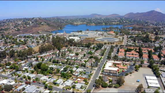 Wide aerial view of a residential and commercial area with hills and a large body of water in the background.