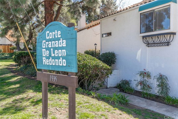 Front view of a white building with a tiled roof and a blue sign reading 'Corte Granada De Leon Redondo'